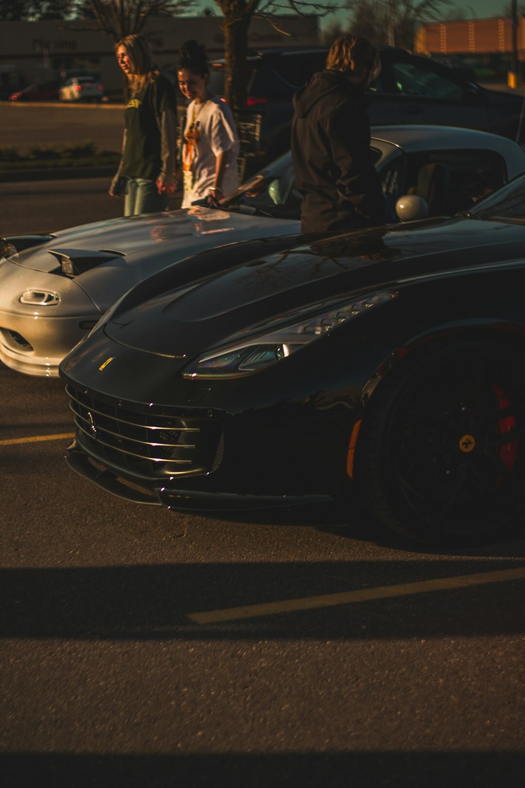 Group of elegantly dressed collectors socializing near exotic cars at an evening event